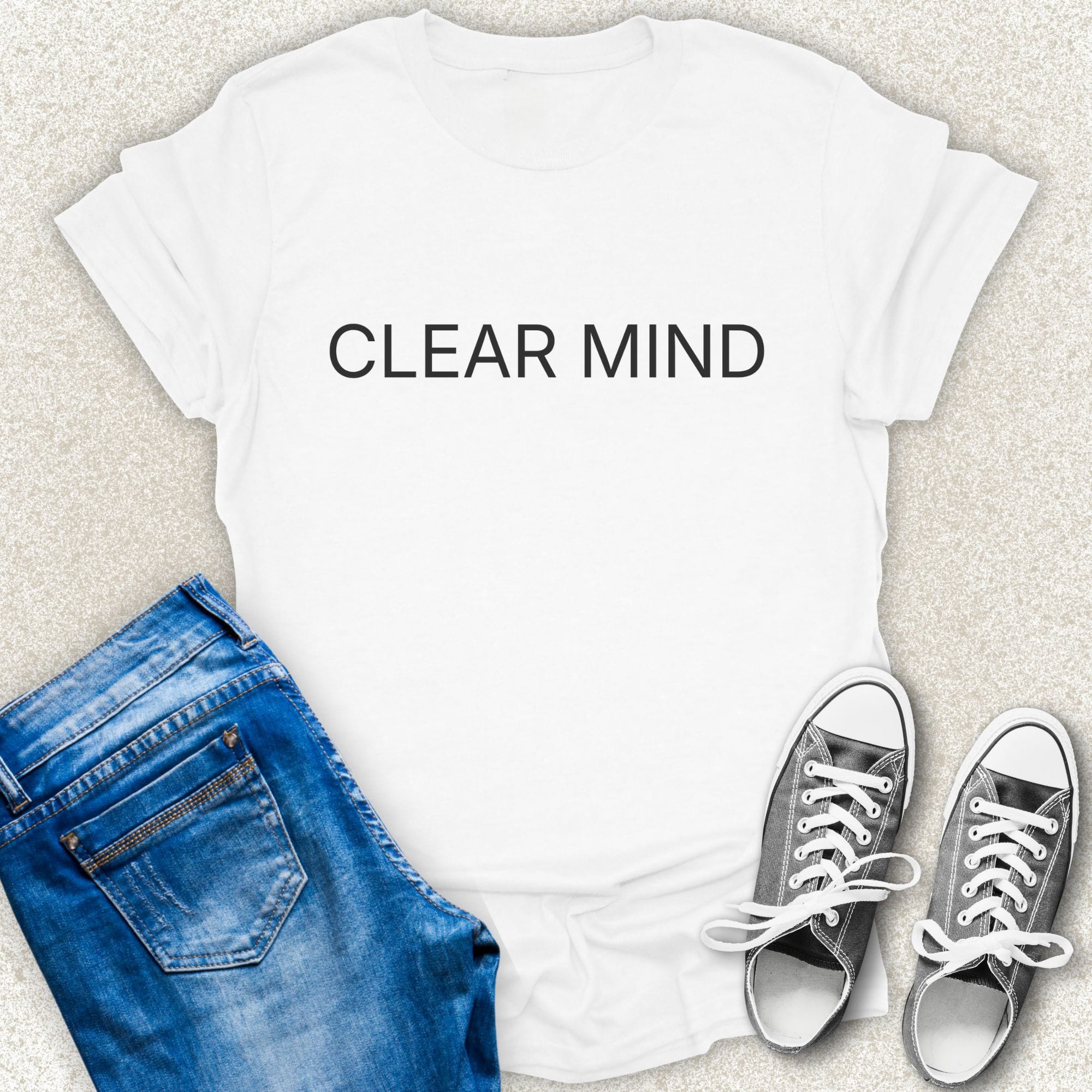 A White short-sleeve T-shirt with the words 'CLEAR MIND' printed in white across the chest, styled in a flat lay with blue jeans and silver sneakers on a light textured background by Low Signal.