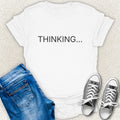An White short-sleeve t-shirt with the word 'STANDBY' printed in white capital letters across the chest, styled in a flat lay with blue jeans and gray sneakers on a light beige textured background by Low Signal